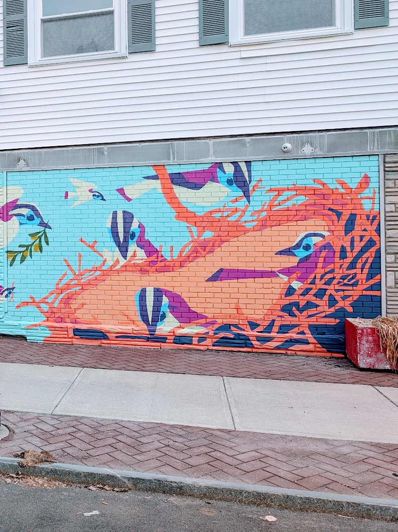The mural on the TAUM building on Second Street in Troy: birds nesting in bright orange branches across a pale blue brick wall.
