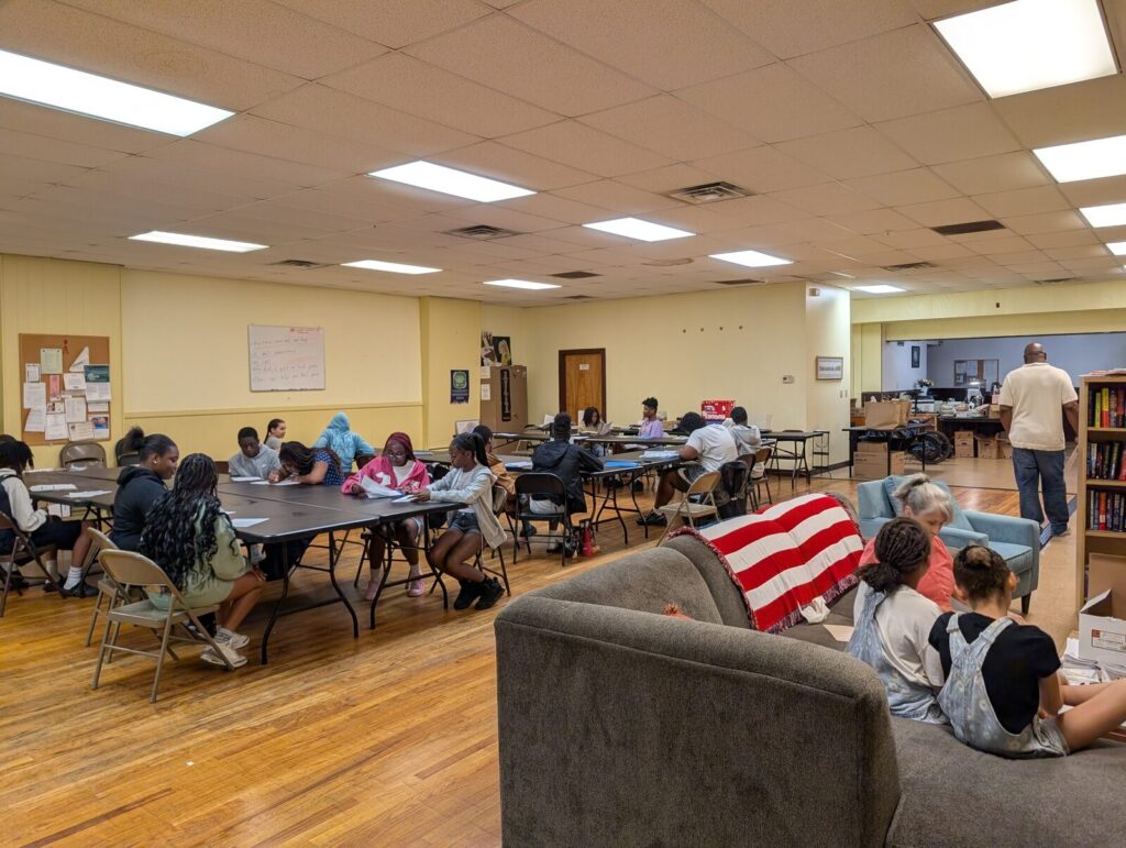 Teenagers spread out across the community room, some at tables and some on couches.