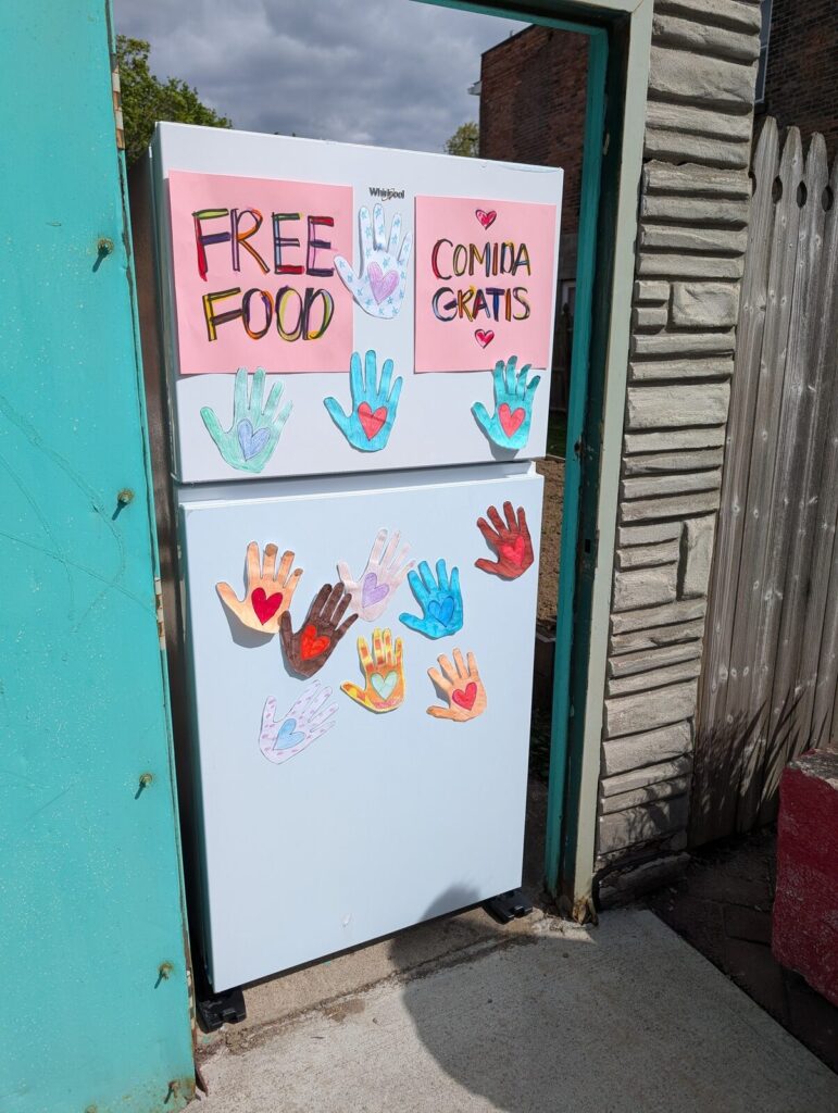 The Free Food Fridge outside TAUM, marked Free Food and Comida Gratis and decorated with painted handprints.