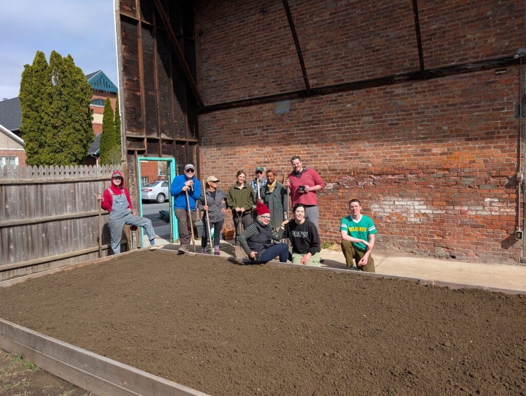 The volunteer crew gathered in the finished community garden beside the brick wall.