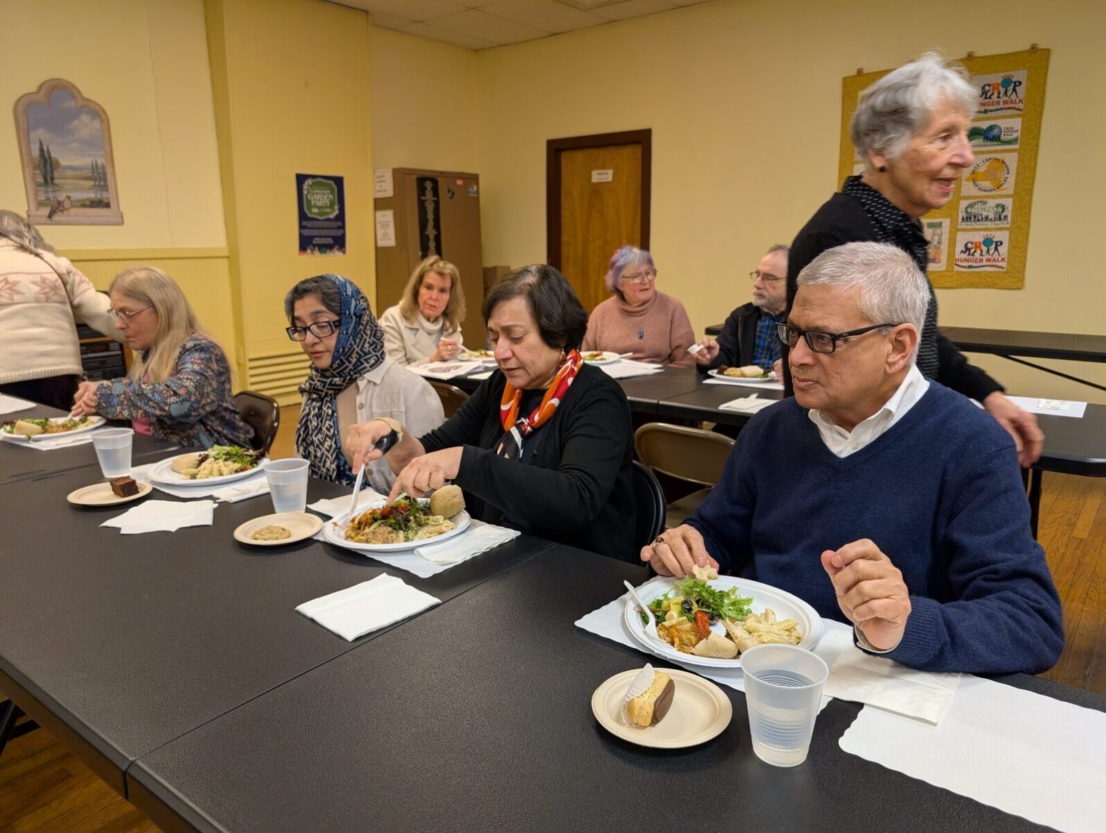 Neighbors sitting together over plates of food at a community meal.