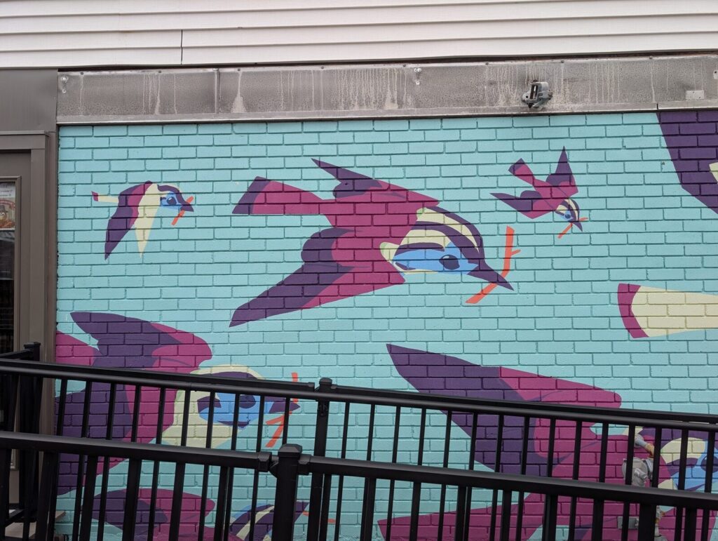 The bird mural on the TAUM building, birds carrying branches across a bright blue wall.