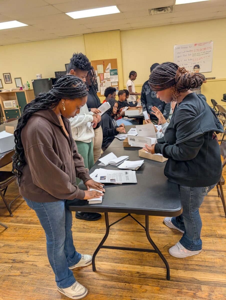 Teens at the Teen Tech Center working together around a table, folding and boxing a mailing.