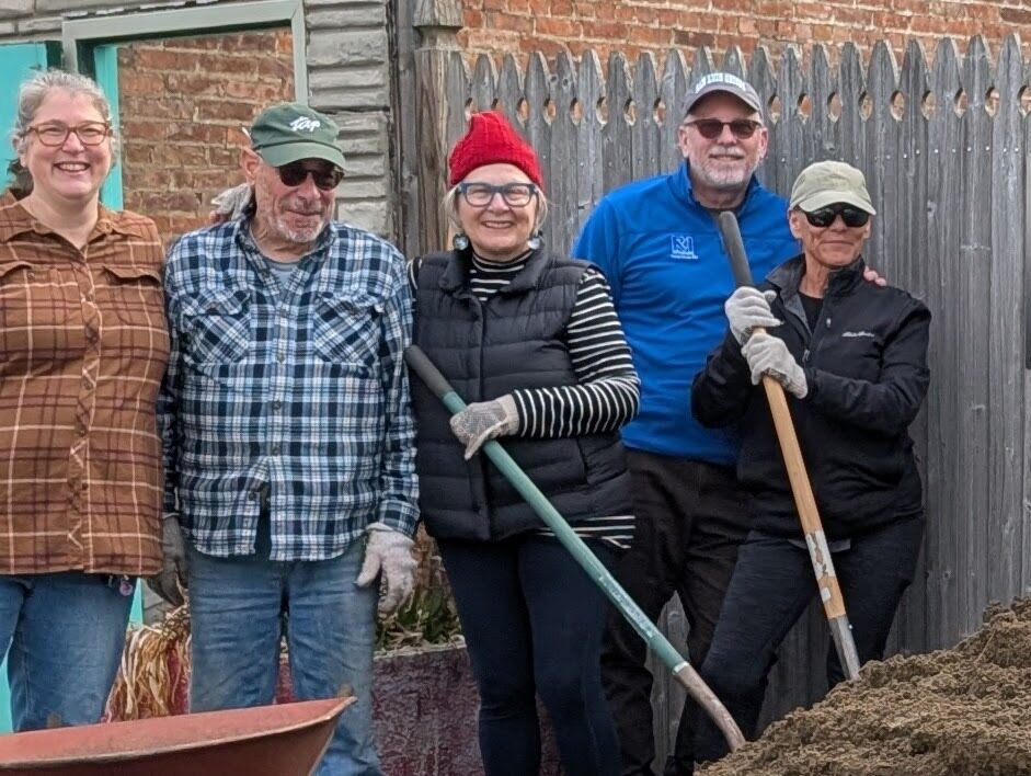 Five volunteers with shovels and a wheelbarrow, smiling at the camera on a work day.